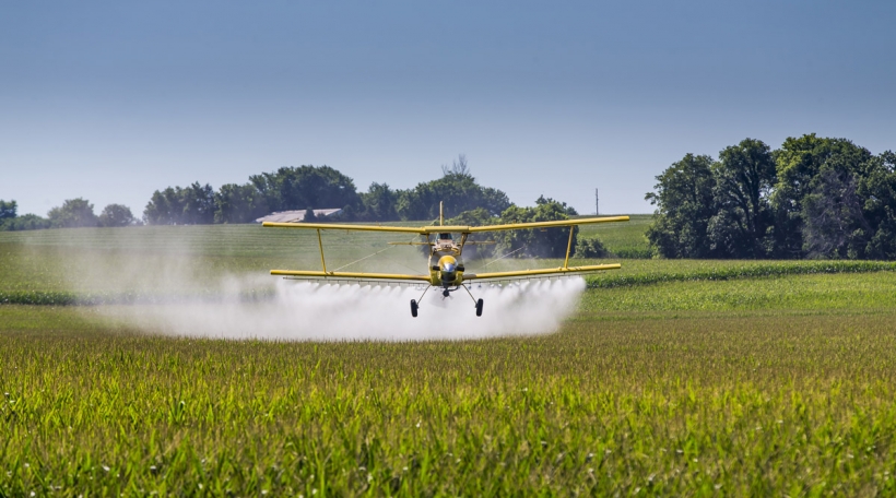 A crop duster applies chemicals to a field of vegetation.